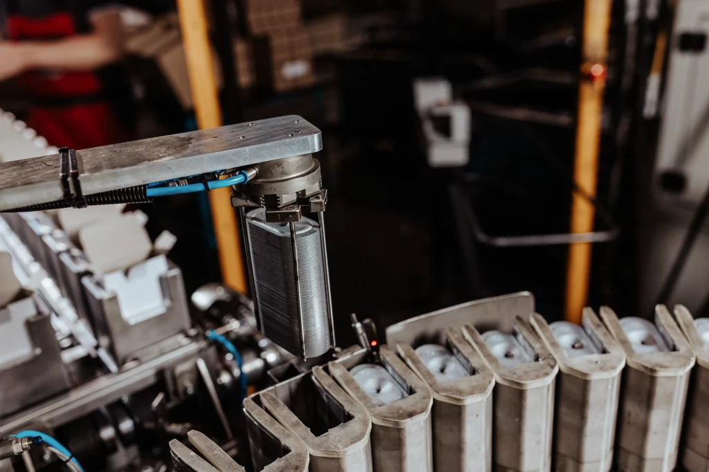 Ein Roboterarm positioniert eine Batteriezelle während des automatisierten Montageprozesses in einer Fabrikumgebung und demonstriert dabei die fortschrittliche Technik und Präzision, die für die Industriefotografie von Fuchs Metalltechnik typisch sind.
