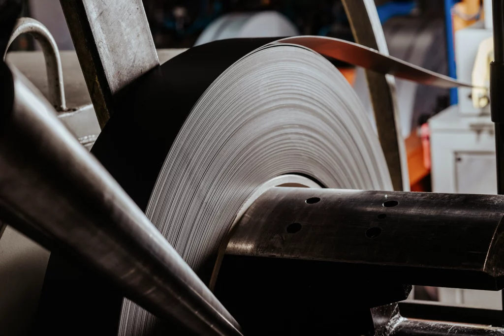 Nahaufnahme einer großen Metallspule, die sich auf einer Maschine in einer industriellen Umgebung abwickelt, vermutlich im Rahmen der Fertigung oder Weiterverarbeitung – ein eindrucksvolles Beispiel für „Technik trifft Handwerk“, eingefangen durch die Industriefotografie bei Fuchs Metalltechnik.