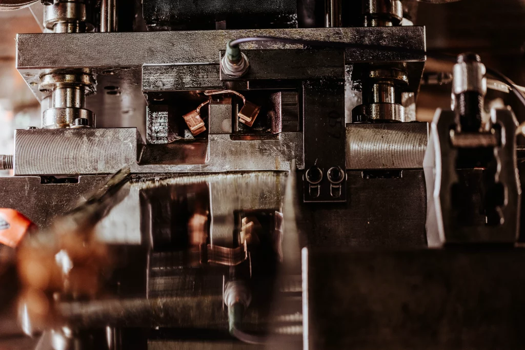 Nahaufnahme von Industriemaschinenteilen mit Metallkomponenten, Verkabelung und reflektierenden Oberflächen in einer Fabrik- oder Werkstatteinrichtung – ein Bild, bei dem Technik auf Handwerk trifft. Diese im Stil der Industriefotografie aufgenommene Szene verdeutlicht die Präzision und Qualität, für die Fuchs Metalltechnik steht.