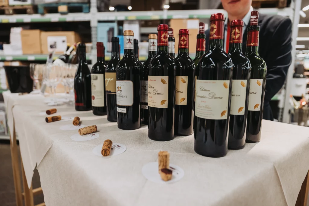 Mehrere Flaschen Rotwein der KASTNER Gruppe stehen in einer Reihe auf einem Tisch, daneben liegen Weinkorken. Diese im Rahmen der Eventfotografie festgehaltene Szene zeigt authentische Momente, wobei im Hintergrund Weingläser und Regale mit Produkten zu sehen sind.