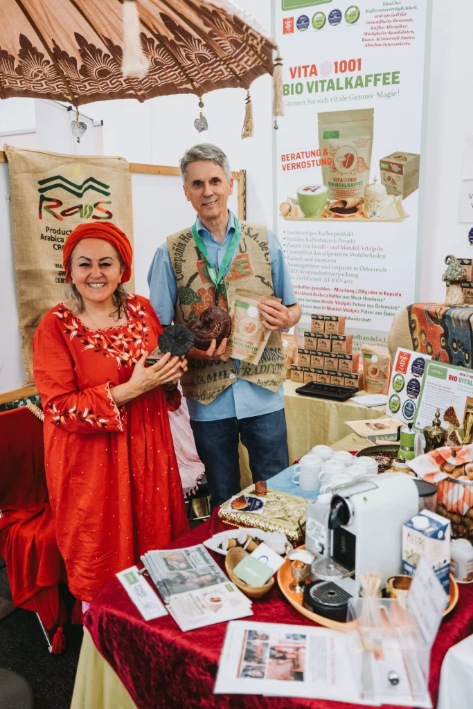 Zwei Personen stehen an einem Stand, an dem Kaffeeartikel und Werbematerialien ausgestellt sind, und vertreten die KASTNER Gruppe. Auf dem Tisch vor ihnen sind verschiedene Artikel und eine Kaffeemaschine angeordnet, die durch professionelle Eventfotografie „echte Momente“ einfangen.
