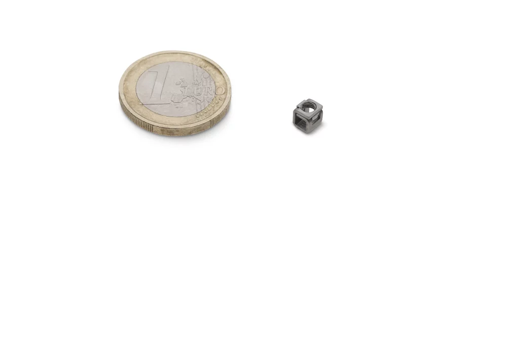 Eine 1-Euro-Münze liegt neben einer kleinen Metallmutter auf weißem Hintergrund, wodurch ein Größenvergleich deutlich wird – eine subtile Anspielung auf „Technik trifft Handwerk“, wie sie in der professionellen Industriefotografie von Fuchs Metalltechnik zu sehen ist.