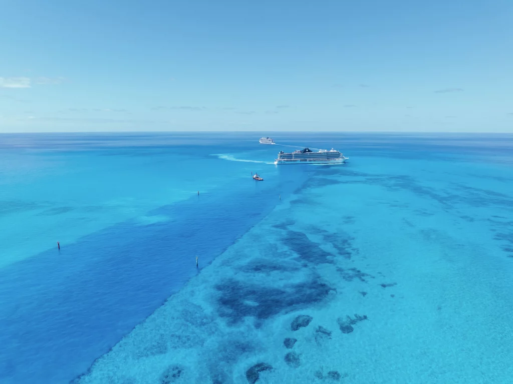 Ein Kreuzfahrtschiff gleitet über klares, türkisfarbenes Wasser, unter dem Korallenriffe zu sehen sind; ein weiteres Schiff ist in der Ferne unter einem strahlend blauen Himmel zu sehen – meisterhaft eingefangen von Imageproduktion.