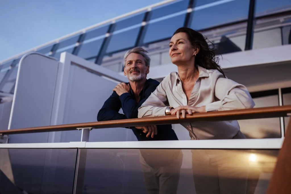 Ein Mann und eine Frau stehen auf dem Deck der MSC World America, lehnen sich an die Reling und blicken in die Ferne, im Hintergrund moderne Glasflächen und der blaue Himmel – ein perfekter Moment aus „Zwei Wochen auf See“ für eine inspirierende Bildproduktion.
